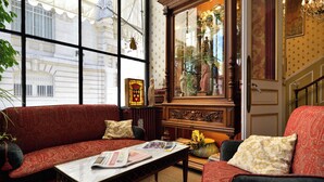 Een gezellige kamer met een rood gestreepte bank, een houten bijzettafeltje met kranten, en een groot raam met uitzicht op een gebouw.