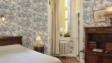 A bedroom with a bed, a nightstand, a lamp, a wooden dresser, and a window with curtains.