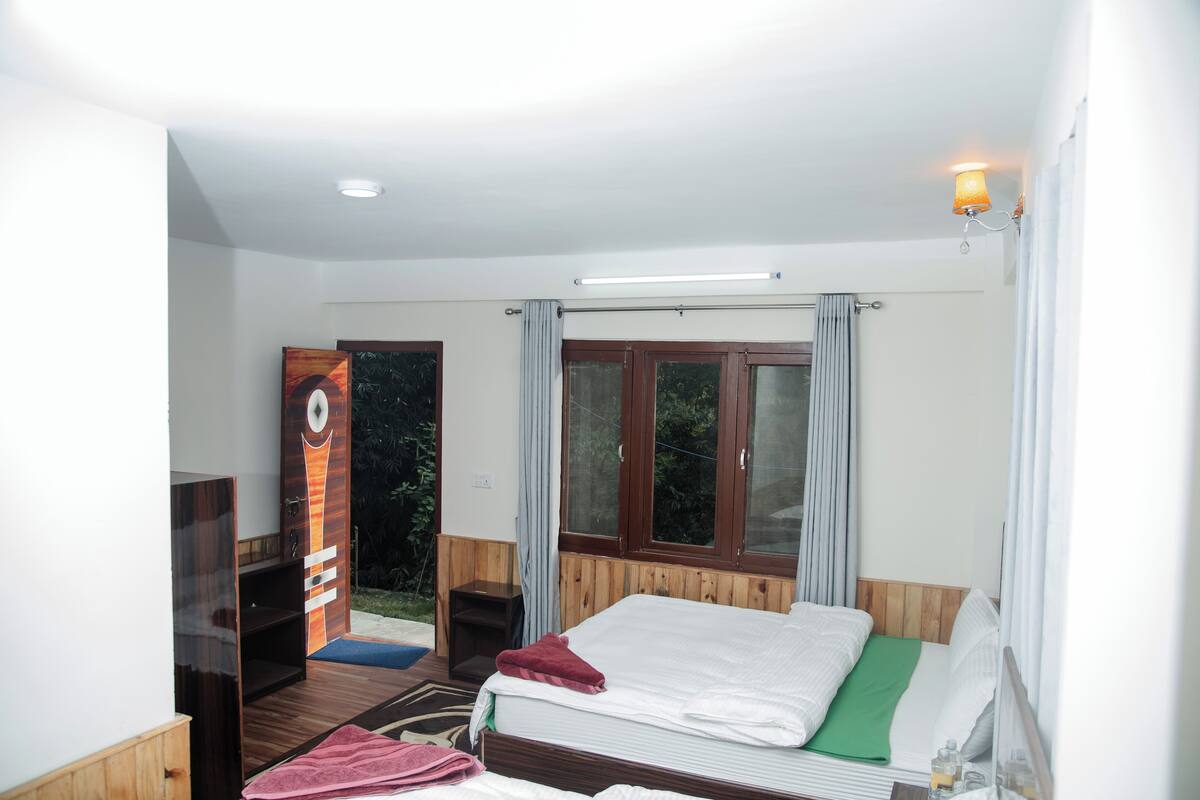Quarto com cama de madeira, uma escrivaninha pequena, uma cadeira e janela com cortinas.