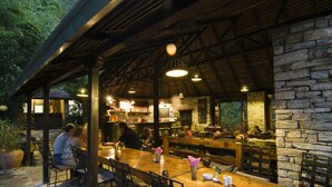 An outdoor dining area with wooden tables and chairs, stone walls, and hanging lights. - The Last Resort (Listikot)