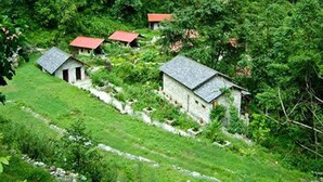 A rural setting with several stone buildings with sloped roofs, surrounded by lush greenery and trees. - The Last Resort (Listikot)