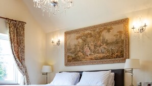 Una habitación de hotel con una cama grande, un candelabro, un cuadro y una ventana con cortinas.