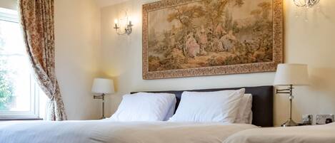 A hotel room with a large bed, a chandelier, a painting, and a window with curtains.