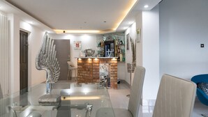 Un comedor moderno con una mesa y sillas de vidrio, una escultura decorativa de un ángel, una pared de ladrillo decorativa y una zona de bar con estantes y botellas.