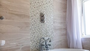 Un baño con una bañera independiente, un cabezal de ducha y una pared de mosaicos.