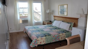 A hotel room with a bed, a desk, a chair, a TV, a window with curtains, a picture on the wall, and a small heater. - Surf Villa Hotel (Ocean City)