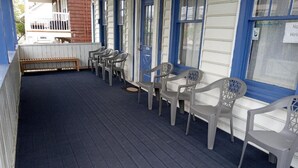 A covered porch with plastic chairs and a bench, wooden floor, and a blue and white building facade. - Surf Villa Hotel (Ocean City)