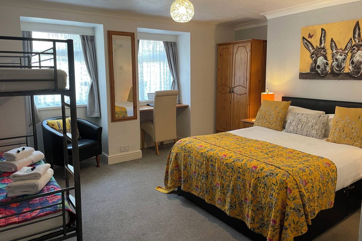 Een hotelkamer met een stapelbed, een bureau, een stoel, een bed met bloemenbeddengoed, een kledingkast en een schilderij van ezels aan de muur.