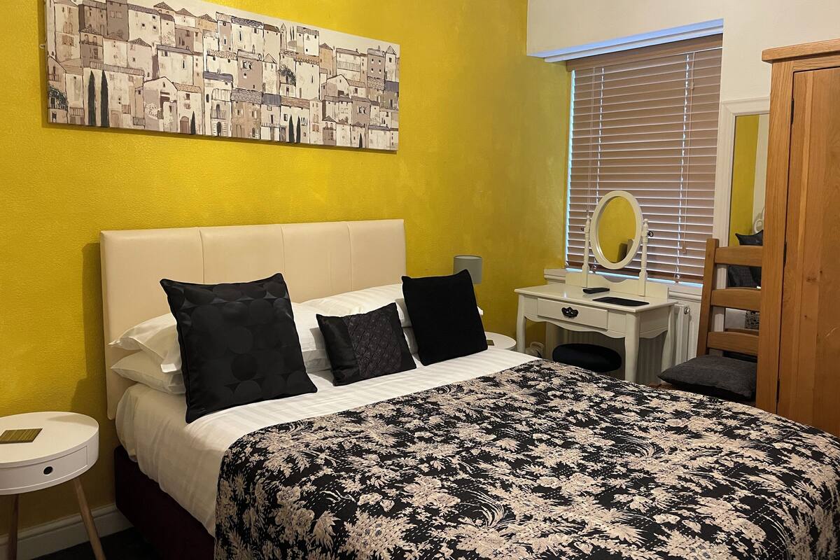 Een hotelkamer met een bed, nachtkastje, dressoir, spiegel en een schilderij aan de muur.