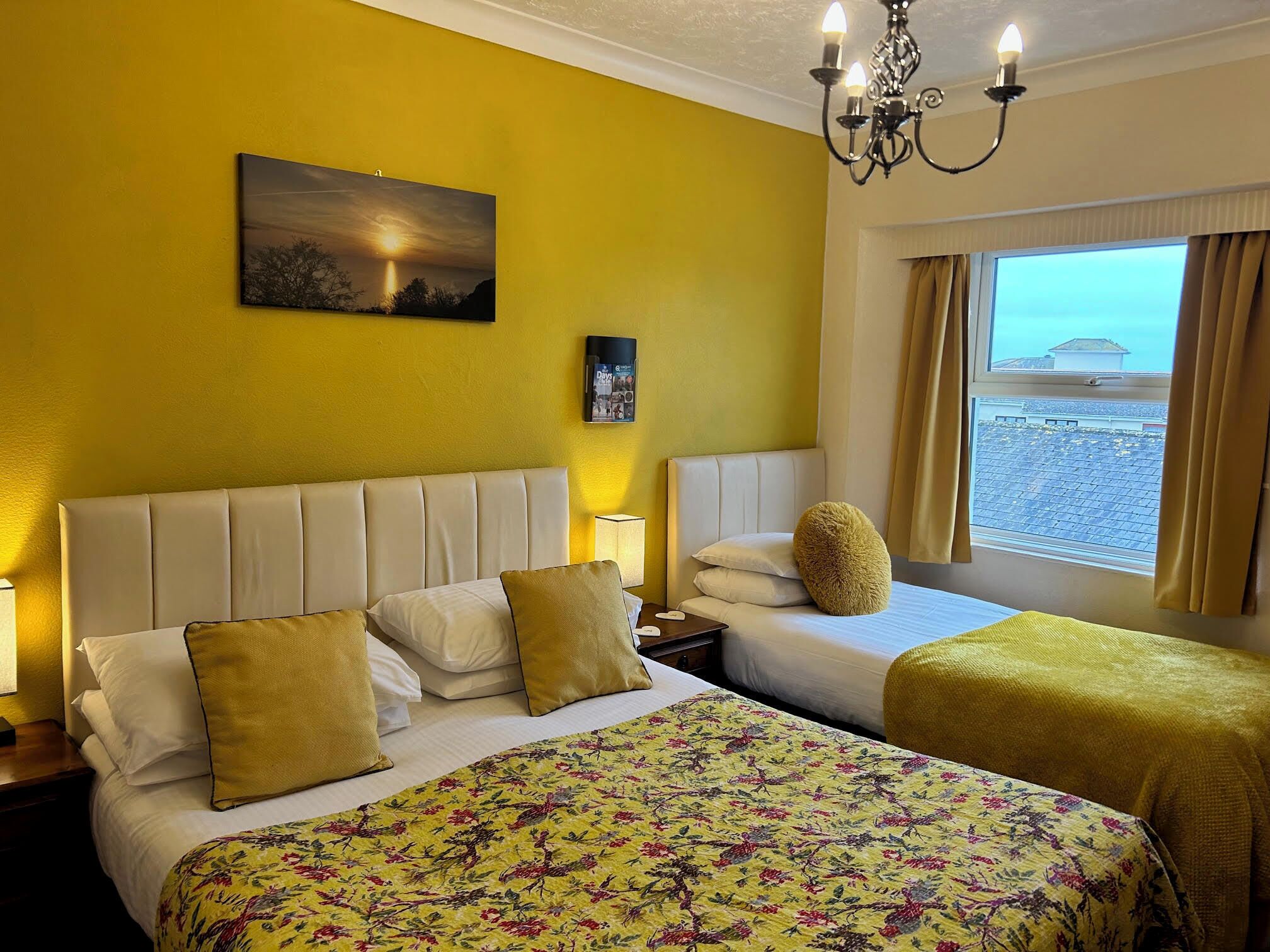 A hotel room with two beds, a large window with a view of the beach, a chandelier, and a painting on the wall.