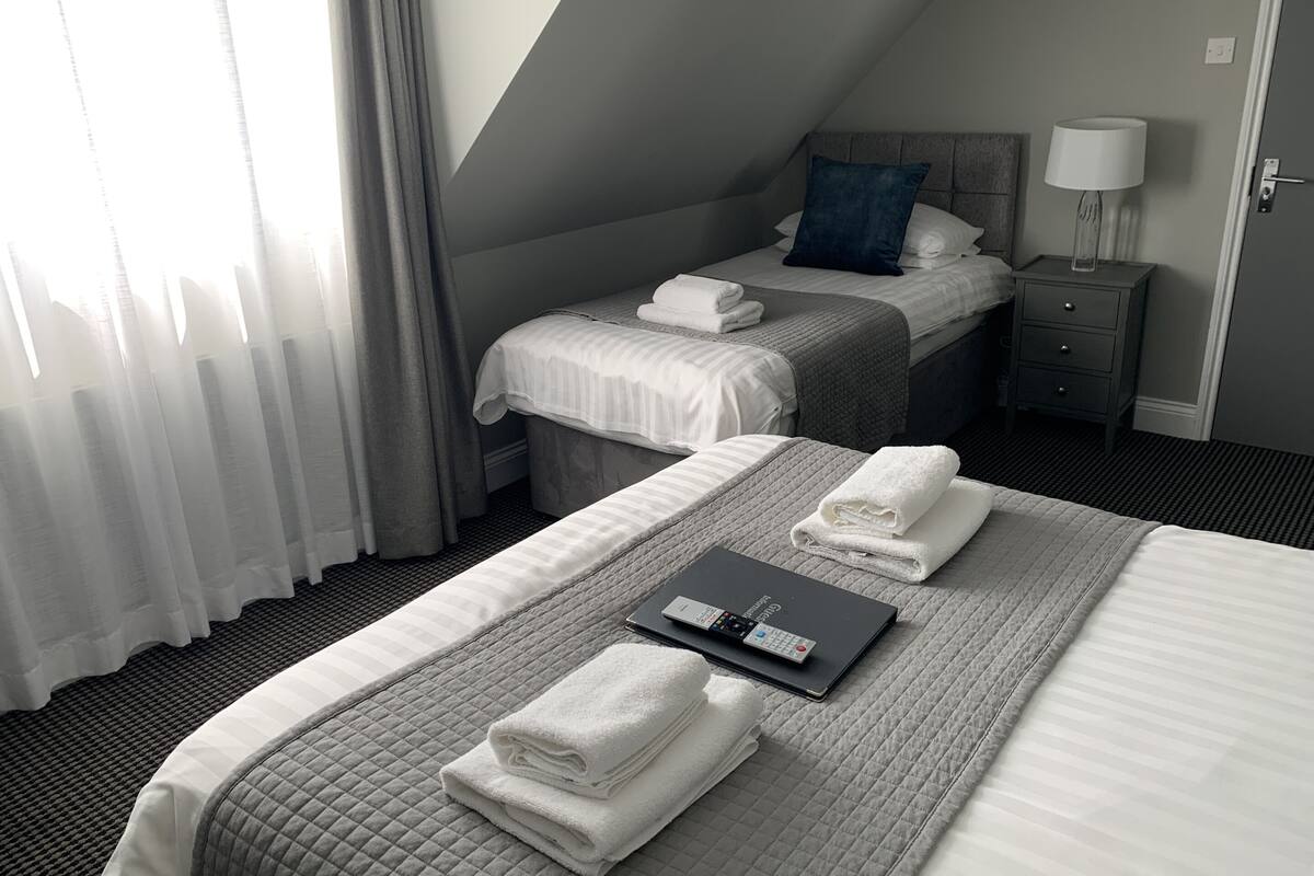 Habitación de hotel con dos camas, una mesita de noche con lámpara y un ordenador portátil sobre la cama.