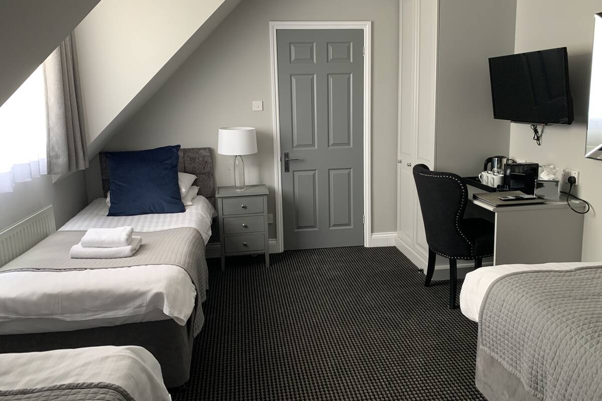 Habitación de hotel con dos camas, un escritorio con una silla, un televisor y una puerta.