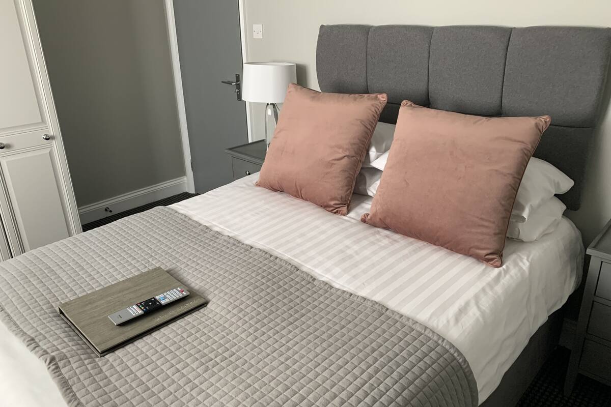 Una cama bien tendida con un edredón acolchado, dos almohadas y un control remoto sobre la cama.