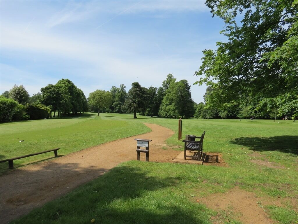 A park with a dirt path, a wooden bench, and a signpost.