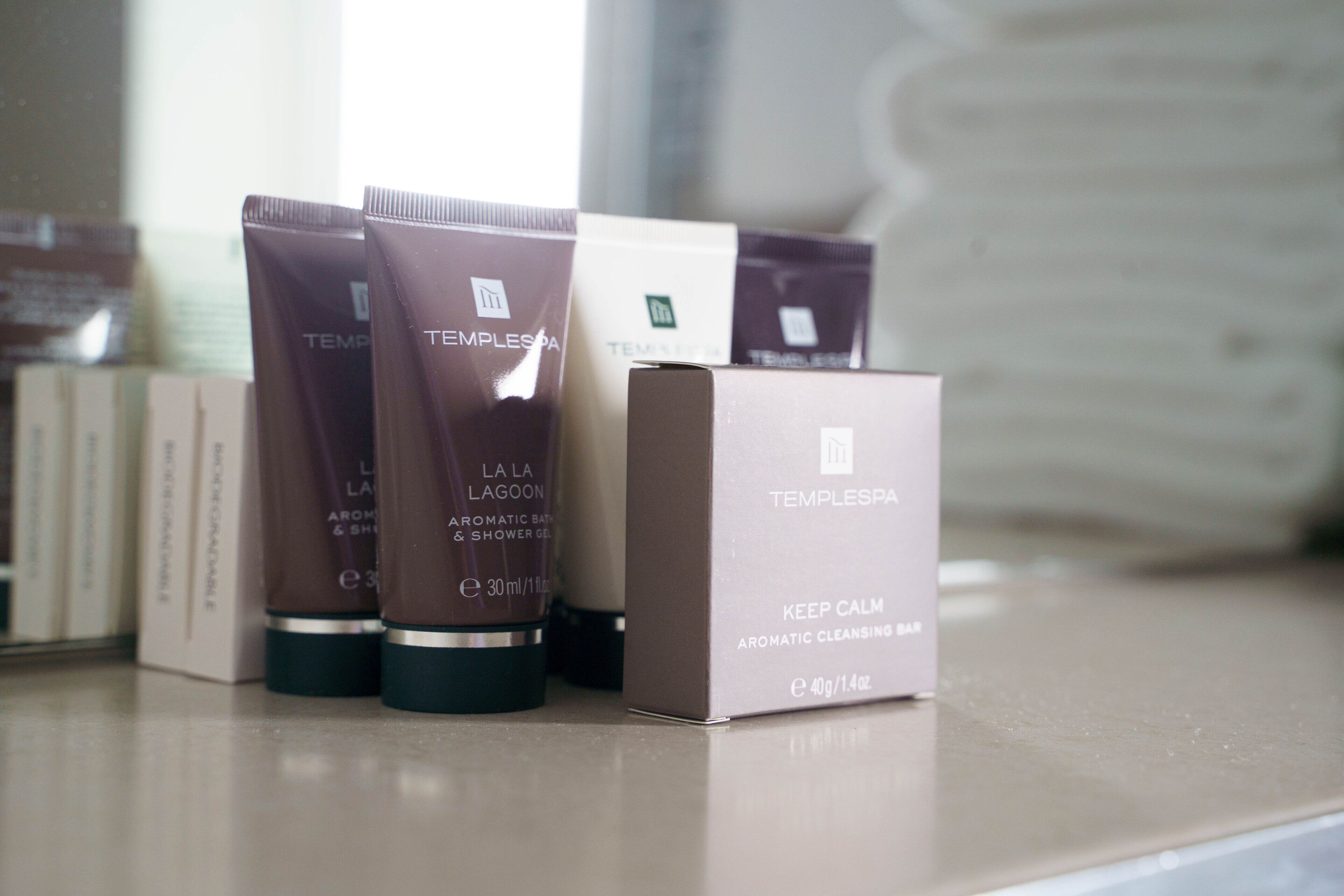 Un juego de artículos de tocador sobre una encimera, incluyendo una caja con la etiqueta 'KEEP CALM AROMATIC CLEANSING BAR'.