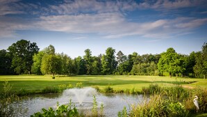 Un campo de golf con un estanque, árboles y cielo despejado.