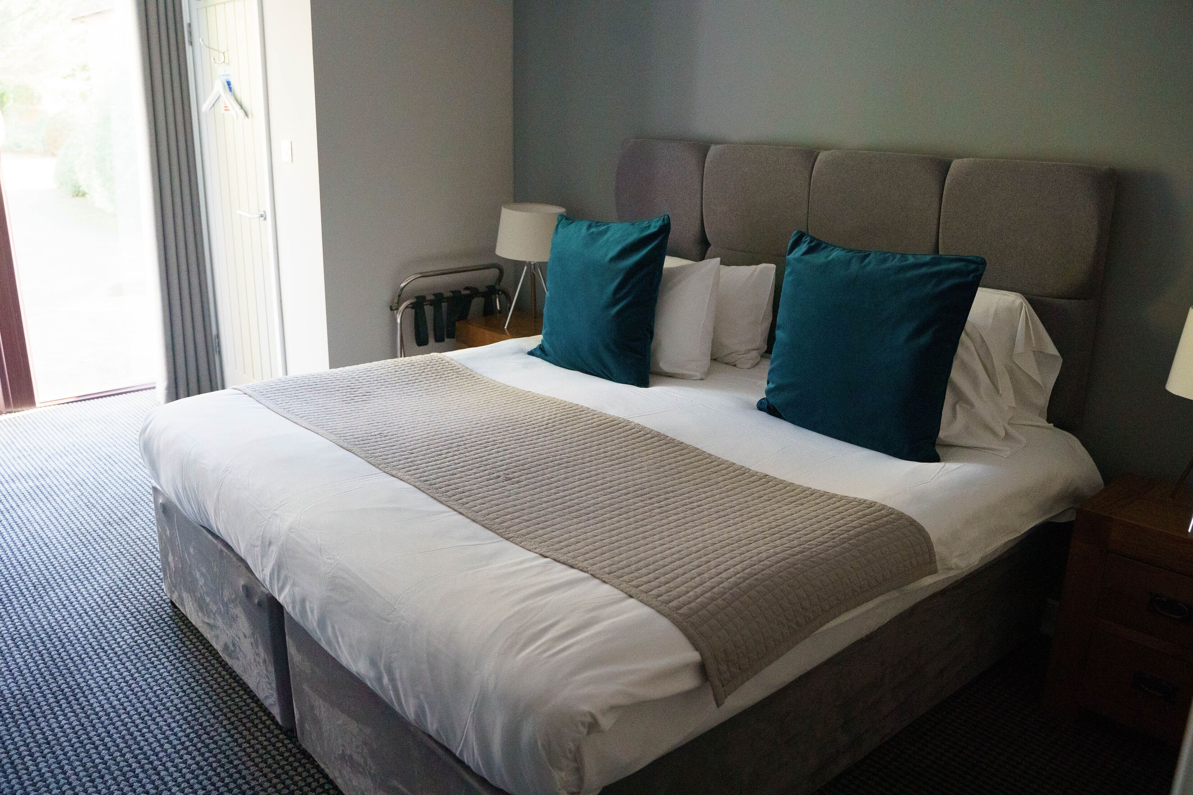 A hotel room with a large bed, grey headboard, and a view of the outdoors through a window.