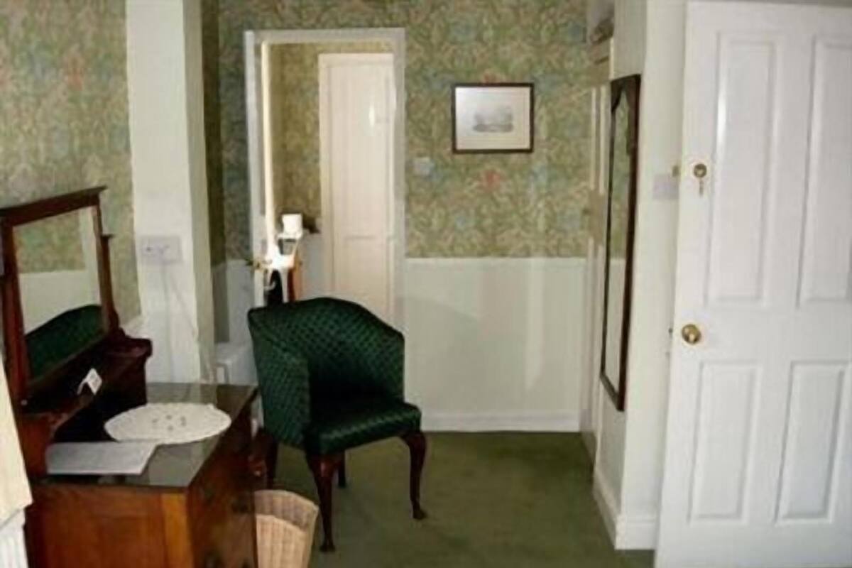 A room with a green armchair, a wooden dresser, a white door, and a framed picture on the wall.