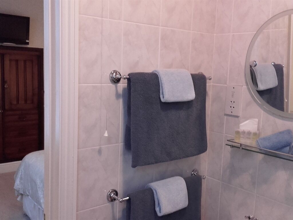 Un baño con dos toallas colgadas en un perchero, un espejo y una repisa con artículos de tocador.
