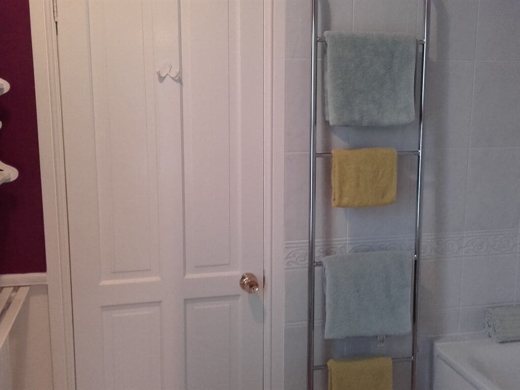 Un baño con una puerta blanca, cabina de ducha de vidrio y un perchero con varias toallas.