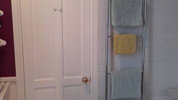 Un baño con una puerta blanca, cabina de ducha de vidrio y un perchero con varias toallas.