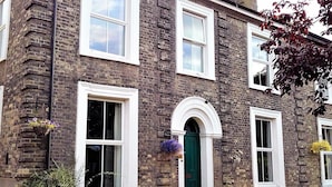 A two-story brick building with white-framed windows, a green door, and flower boxes on the ground floor.