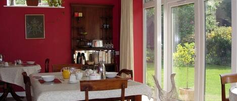 Un comedor con una mesa dispuesta para cuatro personas, un armario de madera y vistas a un jardín a través de amplios ventanales.