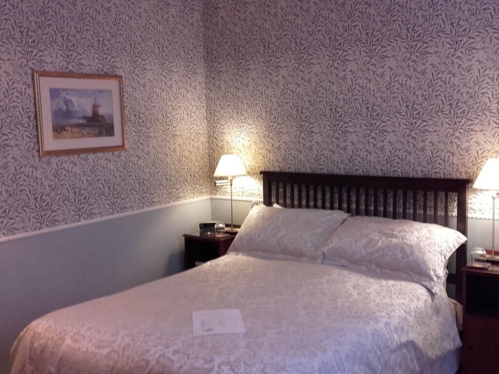 A neatly made bed with a white bedspread, two pillows, and a framed picture on the wall.