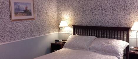 A neatly made bed with a white bedspread, two pillows, and a framed picture on the wall.