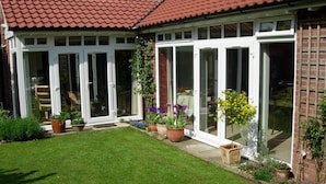 A house with a red-tiled roof, white-framed glass doors, and a well-maintained lawn with potted plants.