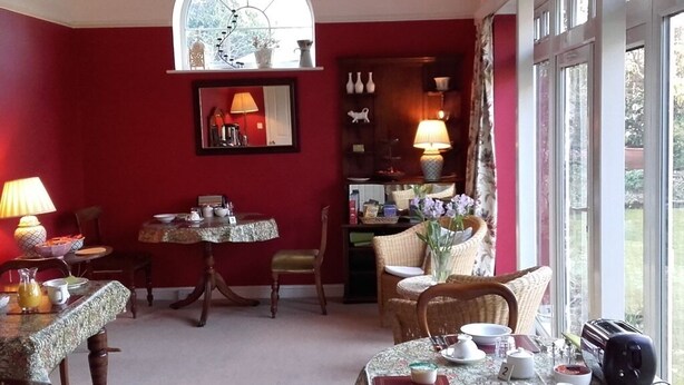 A dining area with a red wall, a large window, and a cozy seating arrangement.