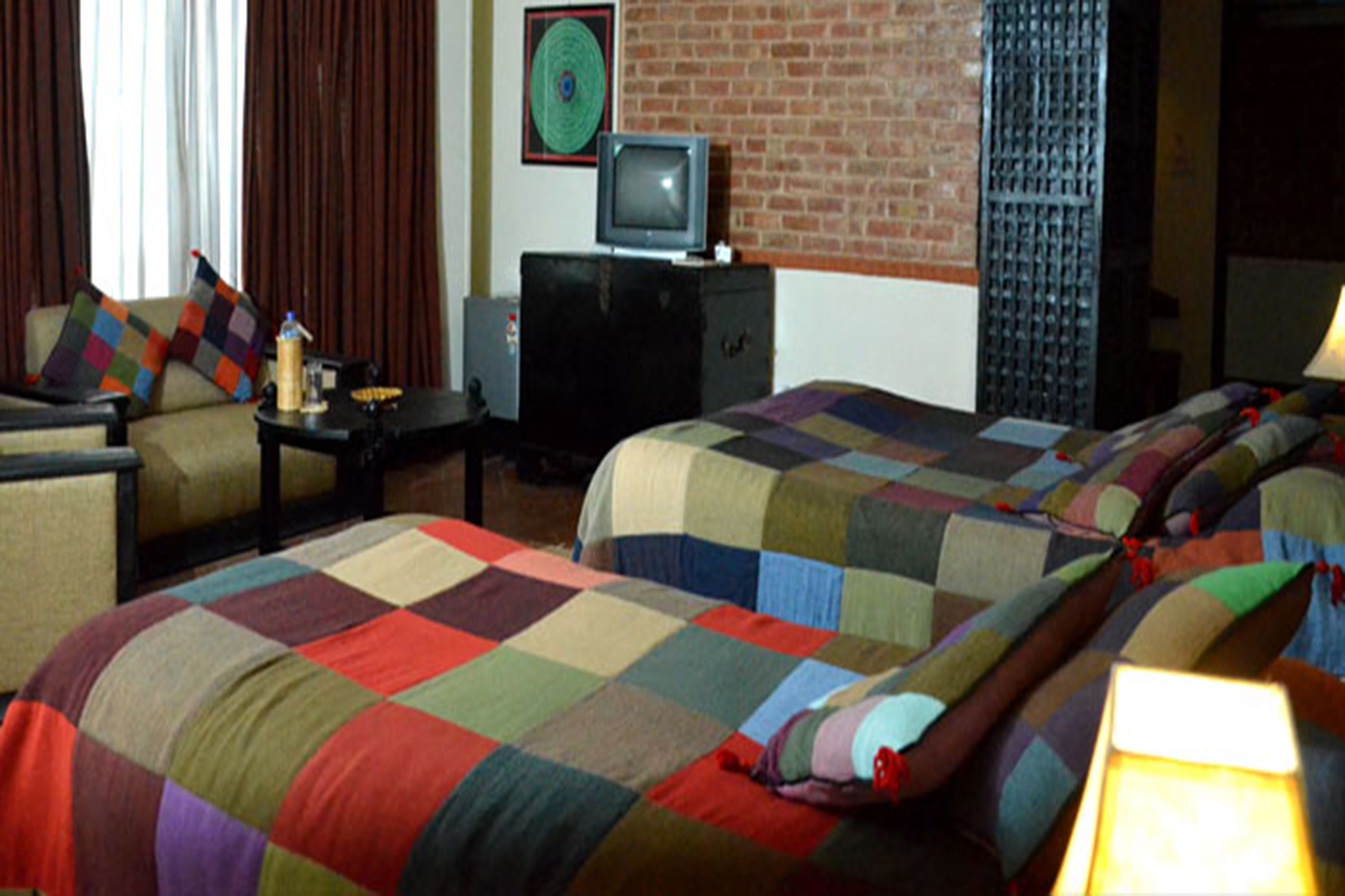 A hotel room with two beds, a television on a dresser, and a brick wall.