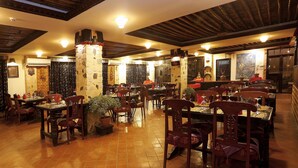 A restaurant with multiple tables and chairs, stone pillars, and a tiled floor. - Hotel Heritage (Bhaktapur)