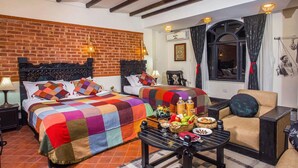 A hotel room with a brick wall, two beds with colorful quilts, a dining table with breakfast, and a view of the city through a window. - Hotel Heritage (Bhaktapur)