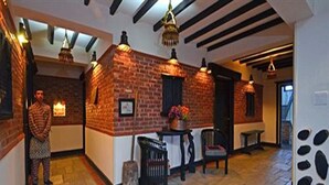 A hallway with exposed brick walls, a stone floor, and hanging pendant lights. There is a bench and a trash can visible. - Hotel Heritage (Bhaktapur)