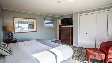 Um quarto com cama, penteadeira, televisão e uma cadeira.