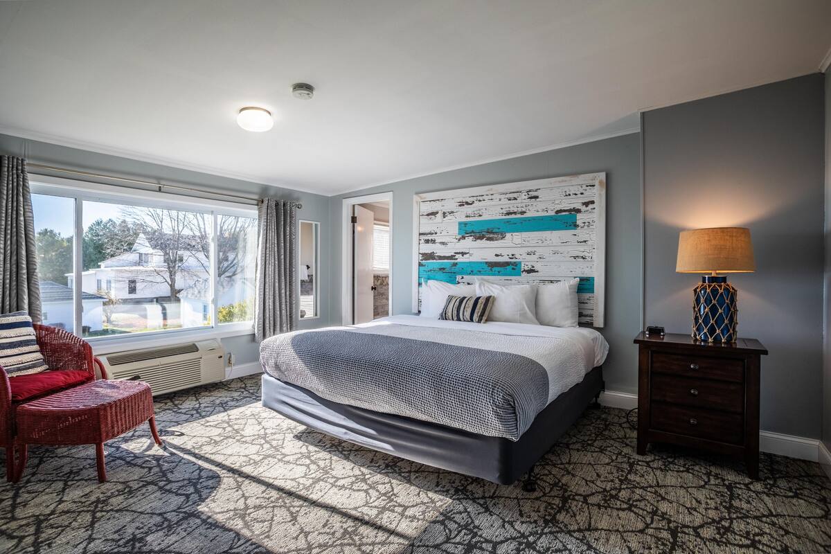A bedroom with a large bed, a nightstand, a chair, and a view of the outside.