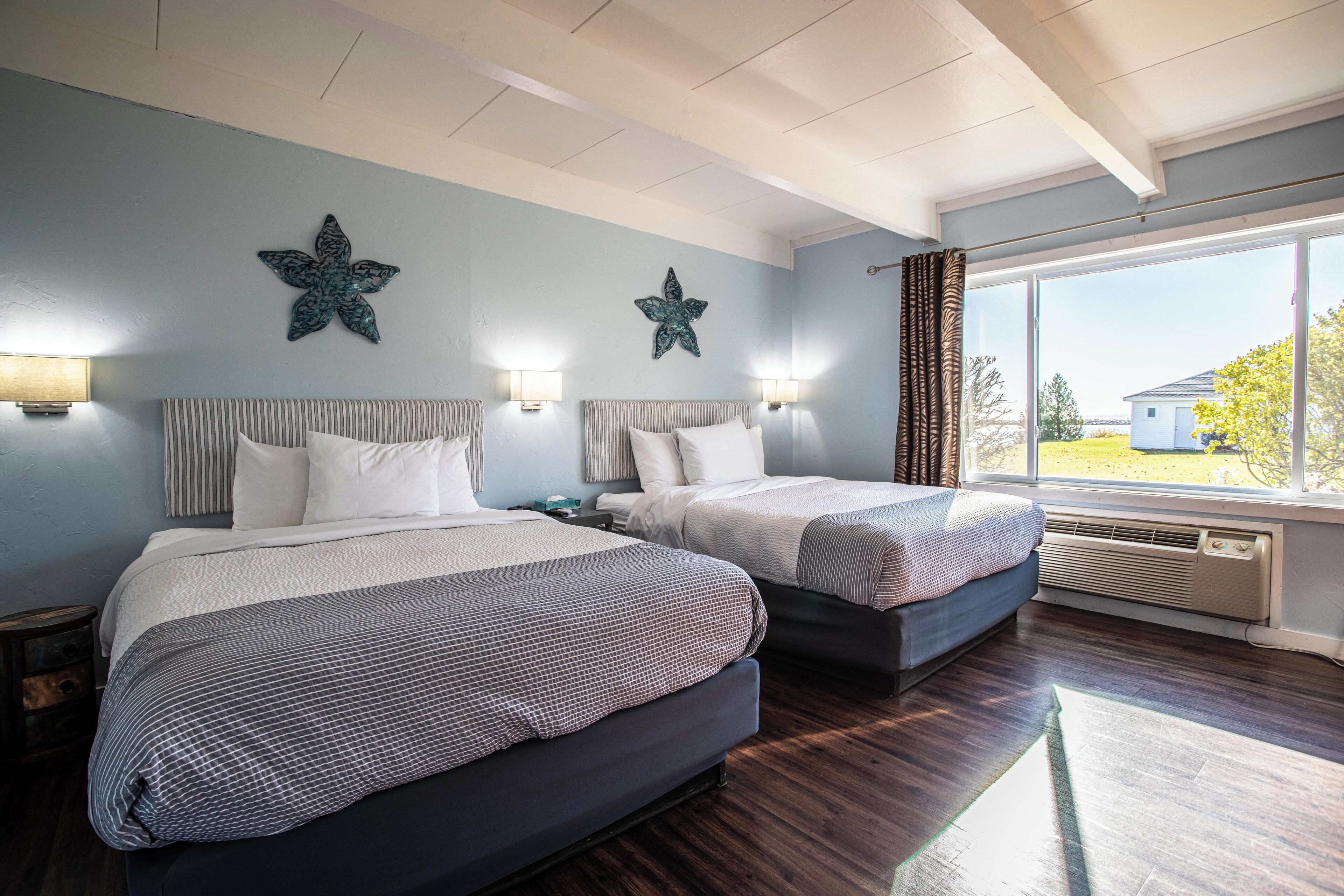 Quarto com duas camas, decoração de parede com estrelas, abajures e uma janela grande com cortinas.