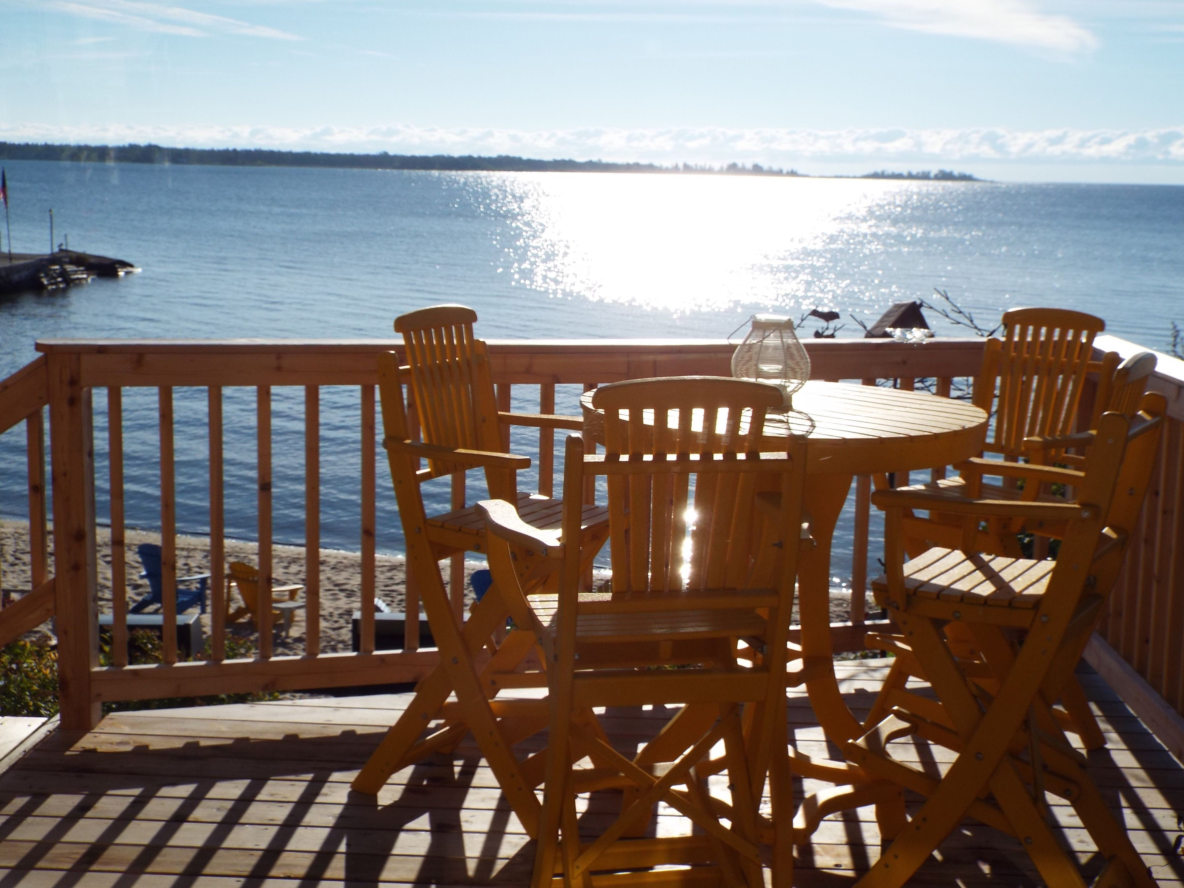 Une terrasse en bois avec une table et des chaises donnant sur une étendue d’eau.