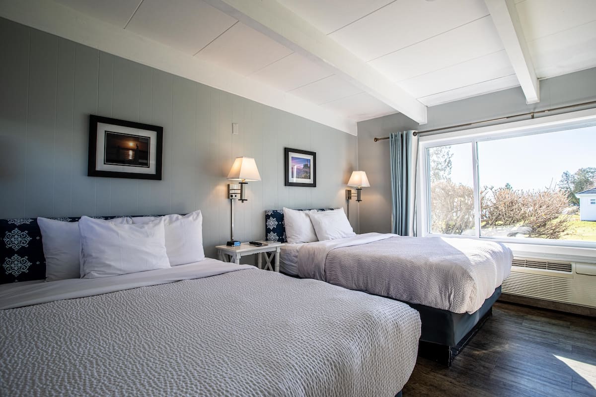 A hotel room with two beds, a large window, and a view of the outside.