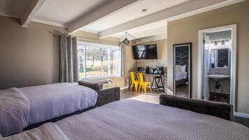 A hotel room with two beds, a TV, a desk with a chair, and a bathroom with a mirror and sink.