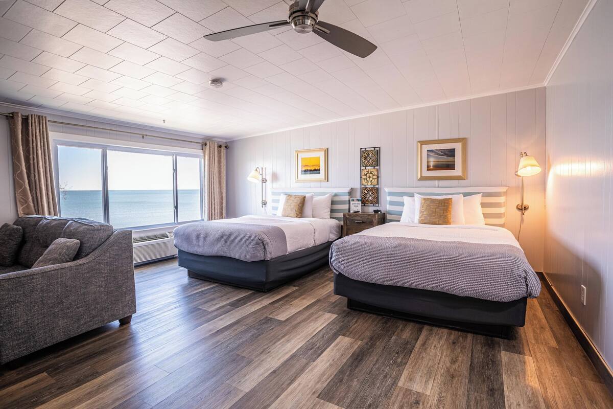 A hotel room with two beds, a sofa, a ceiling fan, and a view of the sea.