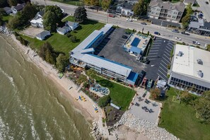 An aerial view of a coastal property with a large building, parking lot, and beach area.