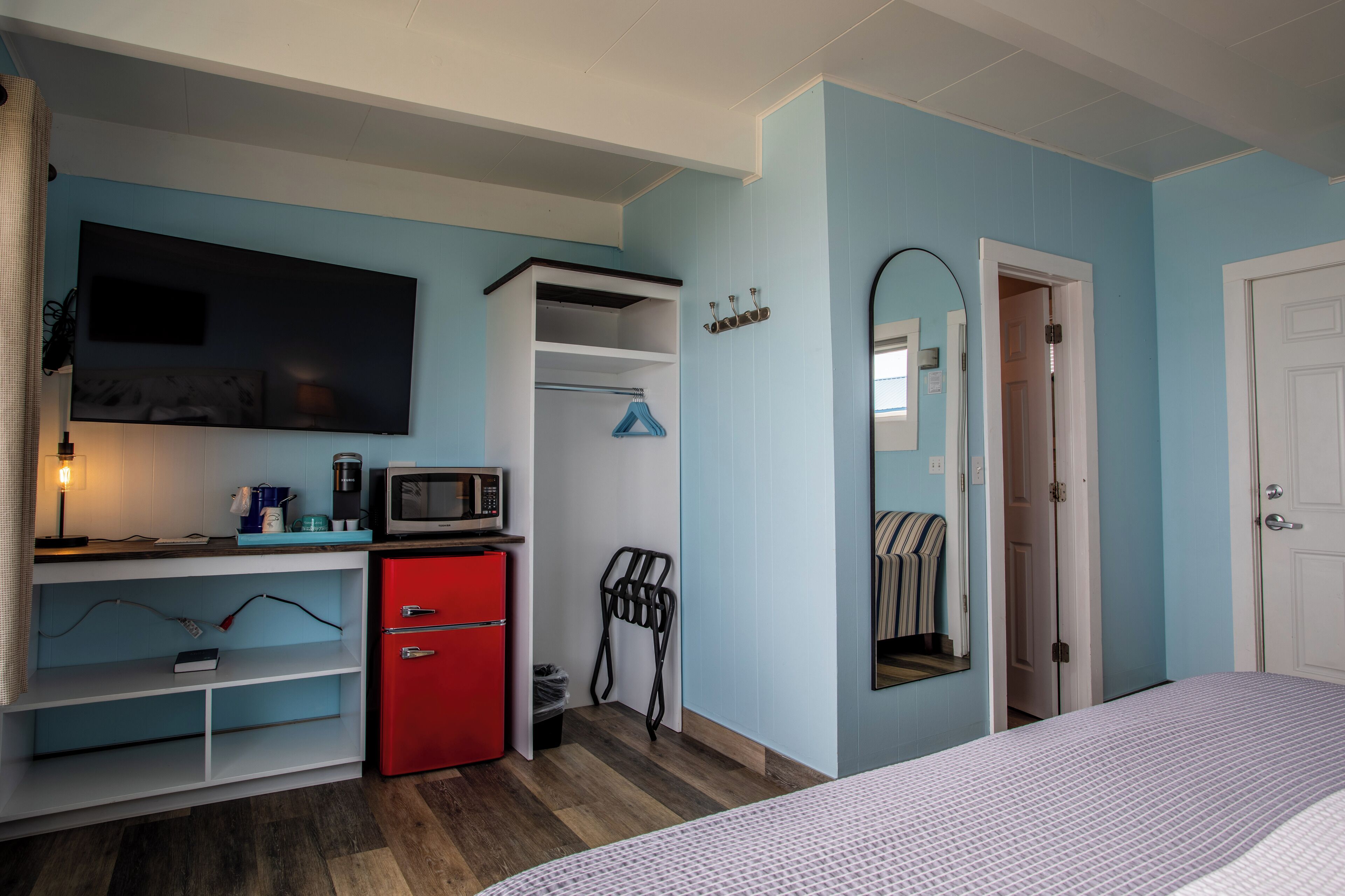 Une chambre avec un lit, une télévision, un mini-réfrigérateur rouge, un four à micro-ondes et un placard avec une tringle pour suspendre les vêtements.