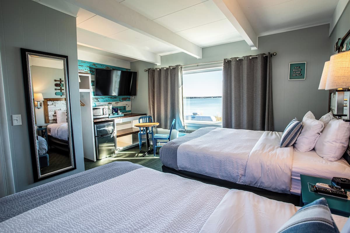 A hotel room with two beds, a kitchenette, a TV, and a view of the sea.