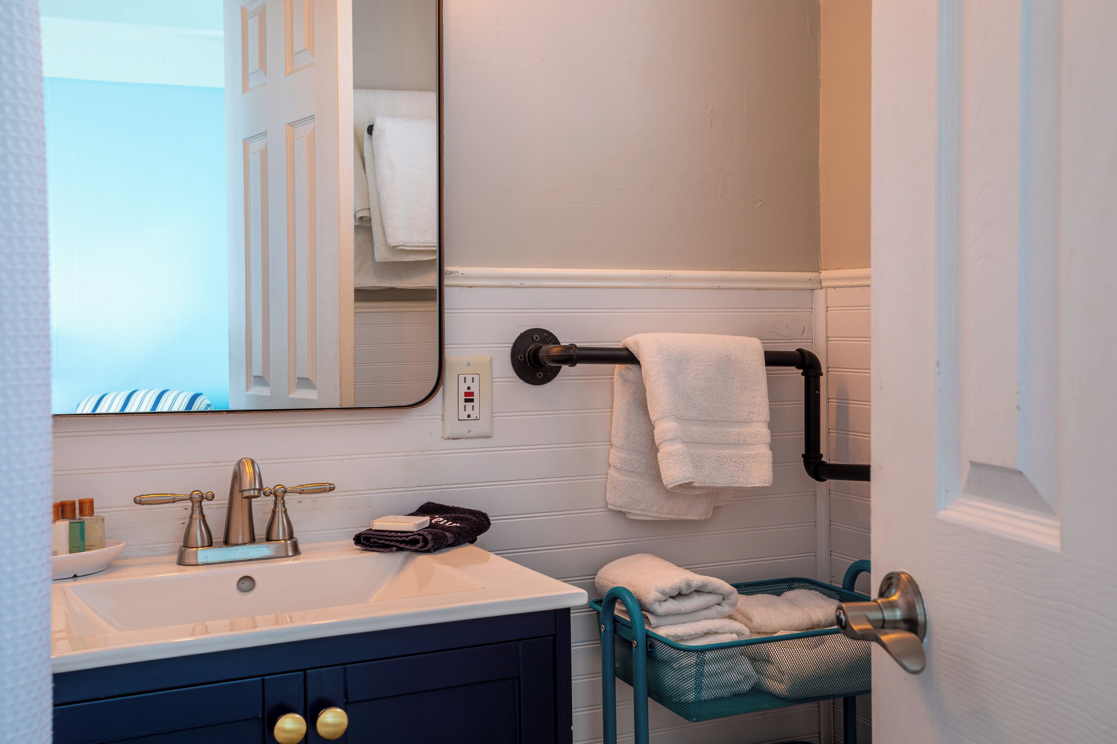 A bathroom with a white sink, a mirror, a towel rack, and a towel basket.