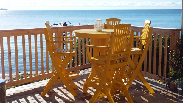 Une terrasse en bois avec des chaises jaunes et une table, le tout offrant une vue sur la mer.