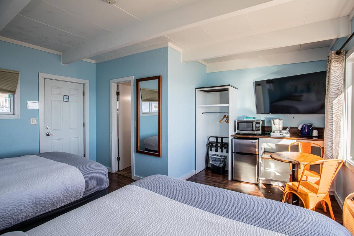 A room with two beds, a desk with a chair, a TV, and a microwave.