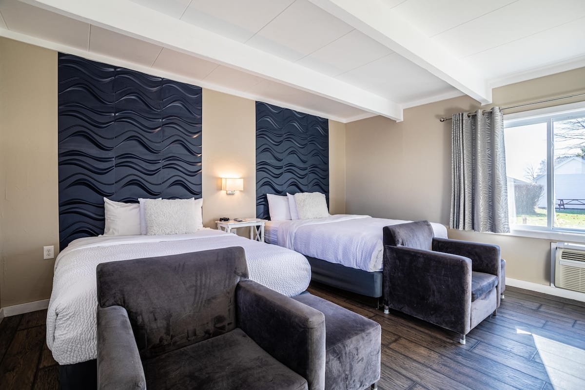 A hotel room with two beds, a desk, and two armchairs.