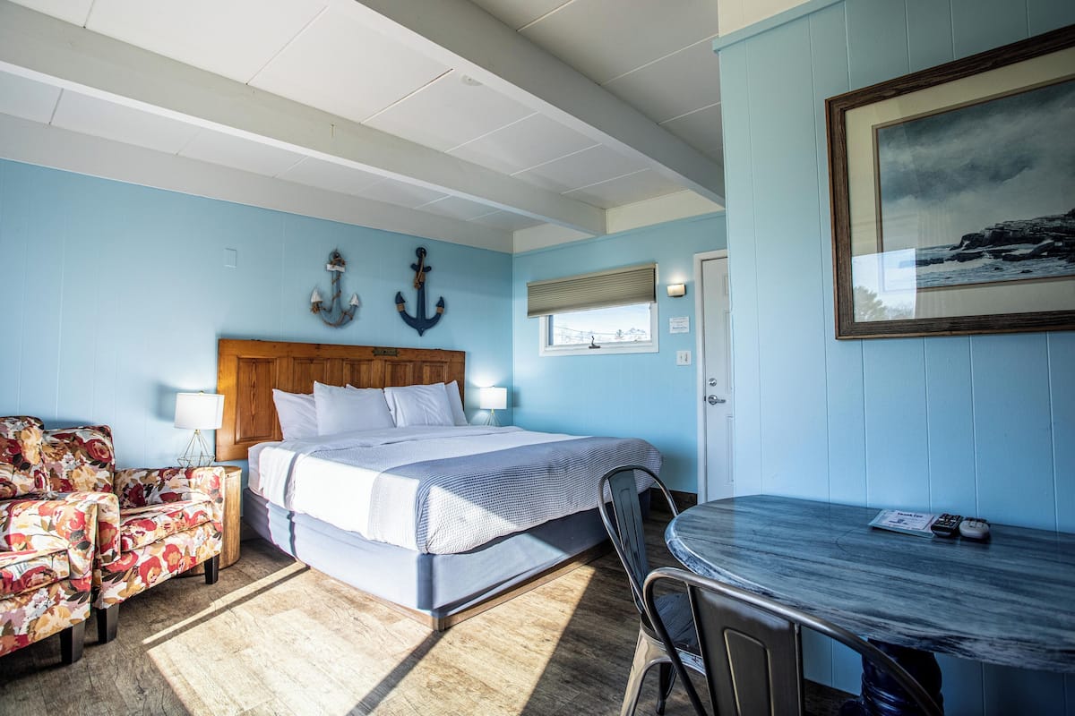 A room with a bed, a chair, a table, and a painting on the wall.